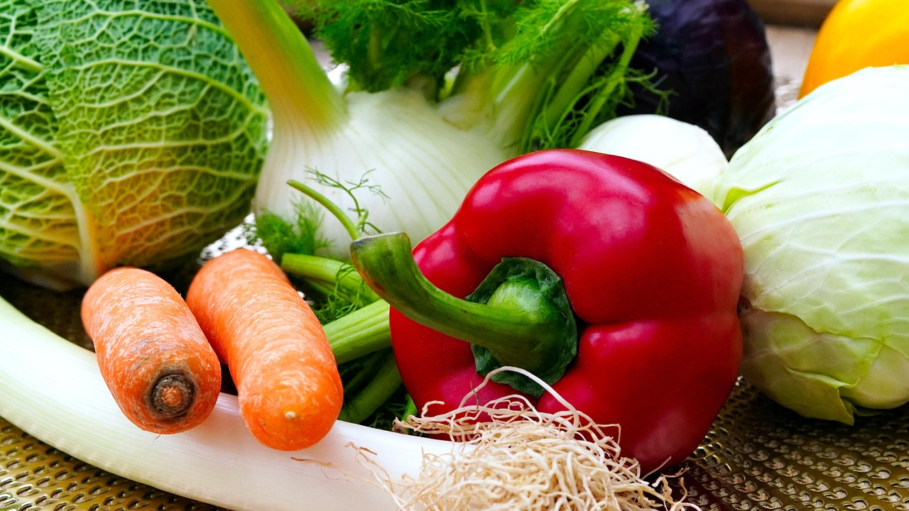 A colorful assortment of freshly harvested vegetables including carrots, red pepper, and fennel from a garden bed.