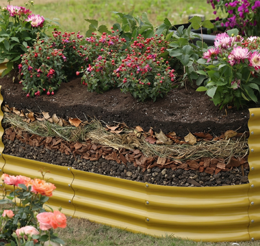 A raised garden bed filled with layered soil and mulch, supporting blooming flowers in an outdoor garden setting.