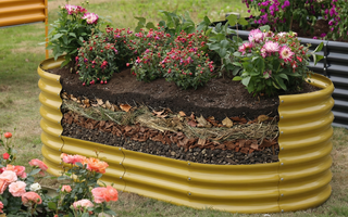A raised garden bed filled with layered soil and mulch, supporting blooming flowers in an outdoor garden setting.