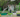 A gardener watering plants in colorful raised garden beds with a hose.