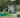 A gardener watering plants in colorful raised garden beds with a hose.