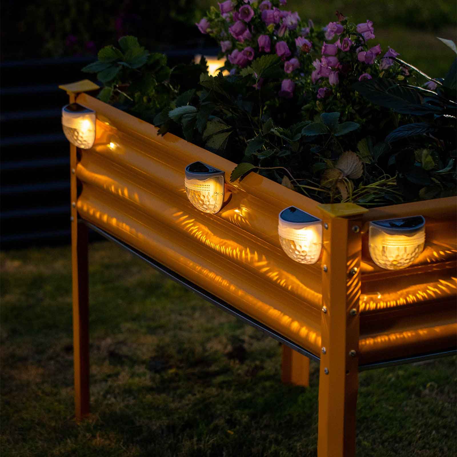 Yellow corrugated galvanized raised garden bed with solar lights and plants at dusk.